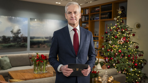 Statsminister Støre står i stua i statsministerboligen. Han holder talekortene han bruker til nyttårstalen. Juletre og møbler i bakgrunnen.
